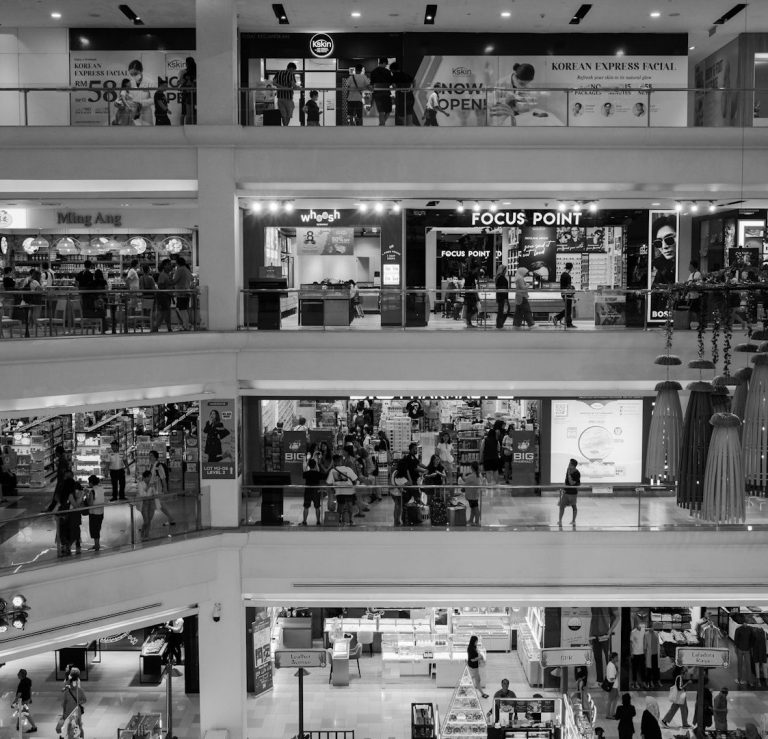 Centro comercial con varias plantas y numerosos compradores en diferentes tiendas.