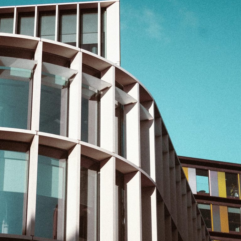 Edificio moderno con fachada curva y grandes ventanales bajo un cielo azul.