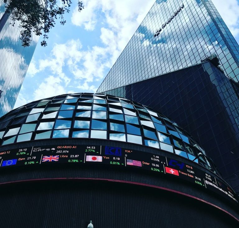 Edificio moderno con pantalla de información financiera y cielo nublado.
